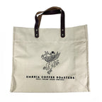 A beige cotton tote bag with leather shoulder straps and a logo printed on the front.